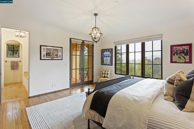 bedroom with access to outside, a notable chandelier, light hardwood / wood-style floors, ensuite bath, and french doors