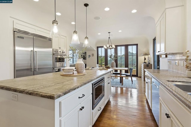 kitchen with white cabinetry, built in appliances, a kitchen island, pendant lighting, and light stone countertops