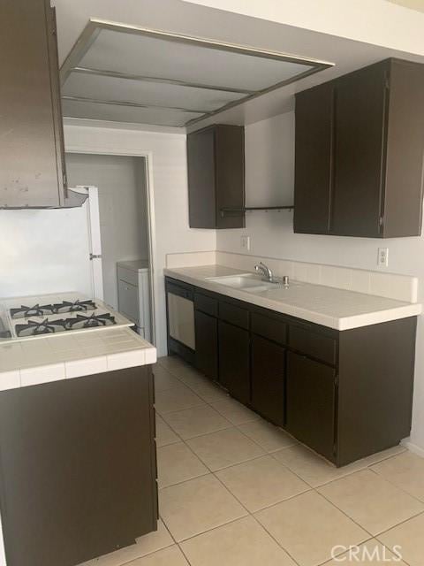 kitchen with light tile patterned flooring, dark brown cabinetry, dishwasher, and sink