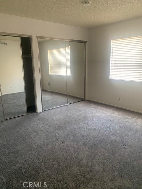 unfurnished bedroom featuring carpet flooring, two closets, and a textured ceiling