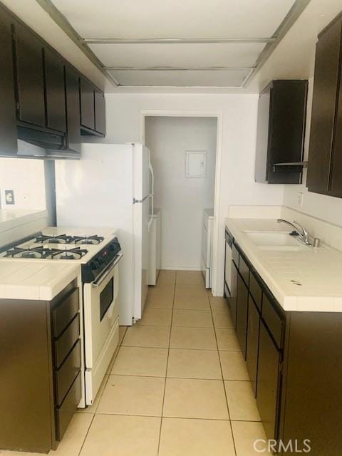 kitchen featuring light tile patterned flooring, sink, white range with gas stovetop, dark brown cabinets, and independent washer and dryer