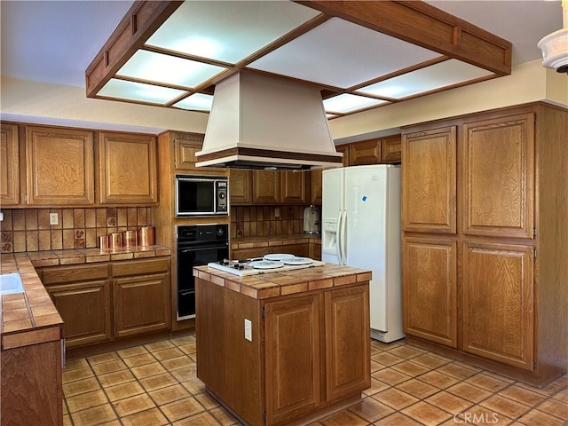 kitchen with white appliances, tasteful backsplash, tile countertops, a center island, and exhaust hood