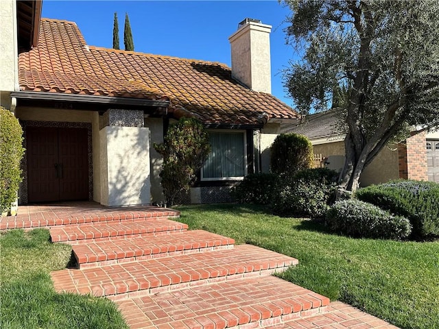 view of front of home with a tiled roof, a front lawn, a chimney, and stucco siding