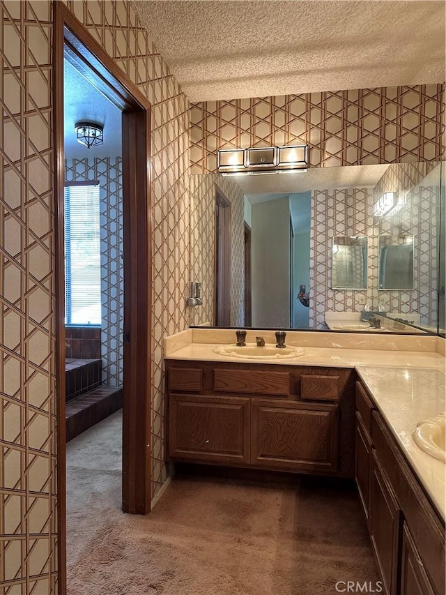 bathroom featuring a textured ceiling, vanity, and wallpapered walls