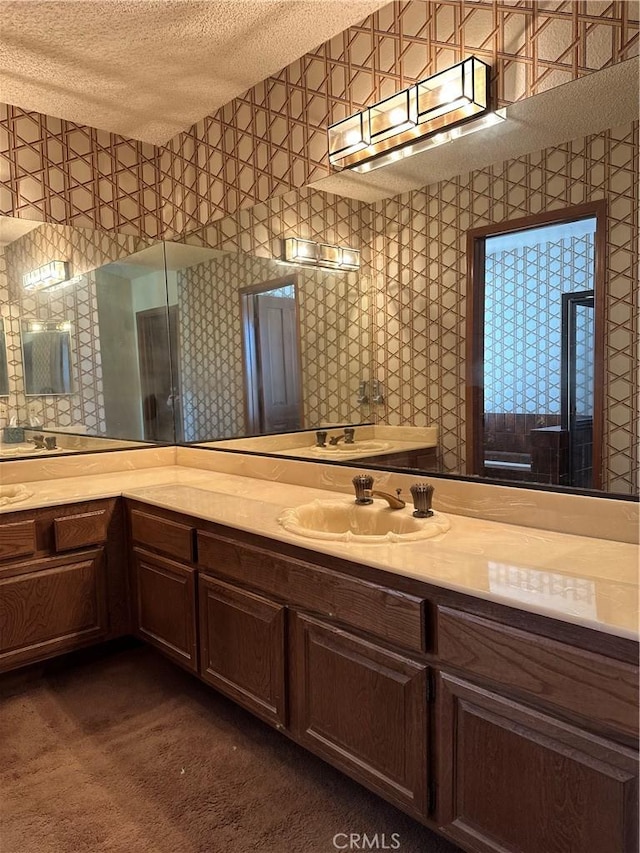 bathroom with a textured ceiling, vanity, and wallpapered walls