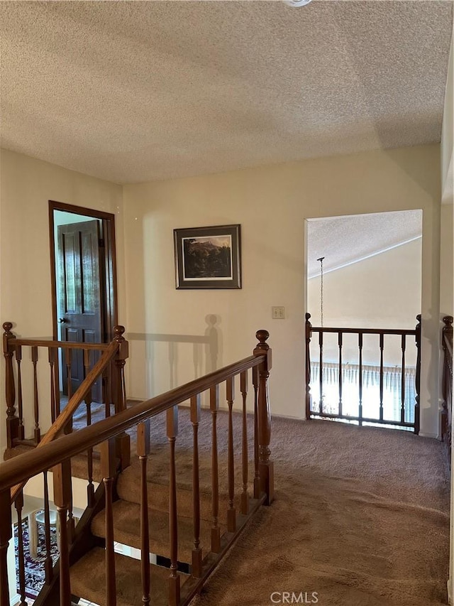 corridor featuring carpet, a textured ceiling, and an upstairs landing