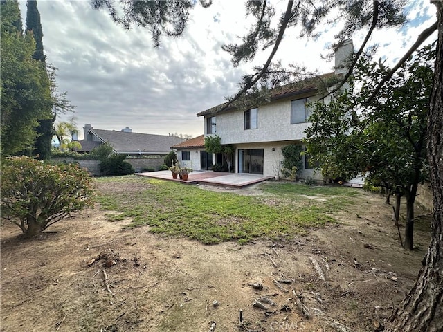 rear view of property featuring a lawn, a patio, a chimney, and stucco siding