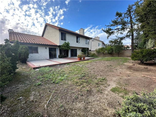 rear view of property featuring a tile roof, a chimney, stucco siding, a patio area, and fence