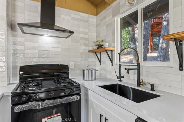 kitchen with black gas range oven, white cabinetry, sink, decorative backsplash, and wall chimney exhaust hood