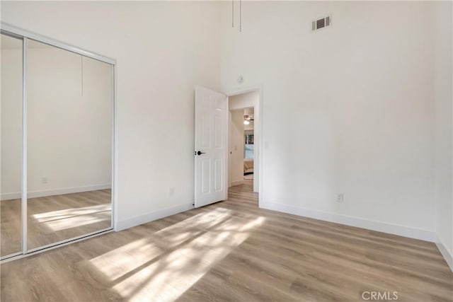 unfurnished bedroom with hardwood / wood-style flooring, a closet, and a high ceiling