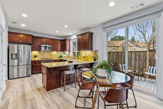 kitchen featuring light hardwood / wood-style flooring, a breakfast bar, stainless steel appliances, light stone countertops, and kitchen peninsula