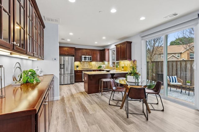 kitchen featuring tasteful backsplash, stainless steel appliances, a kitchen bar, and light hardwood / wood-style flooring