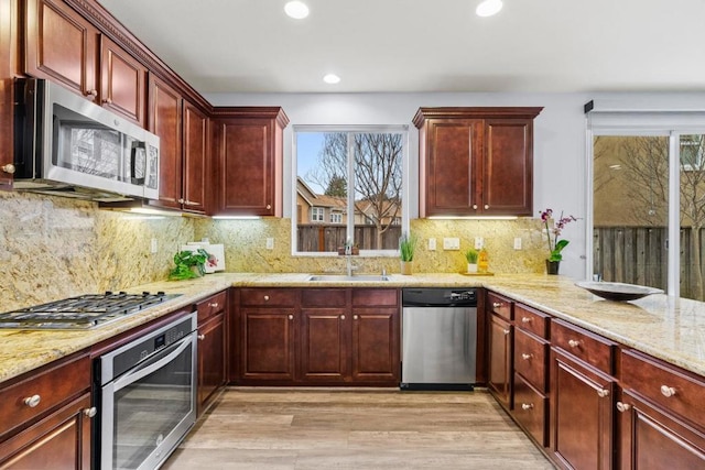 kitchen featuring sink, tasteful backsplash, appliances with stainless steel finishes, light stone countertops, and light hardwood / wood-style floors