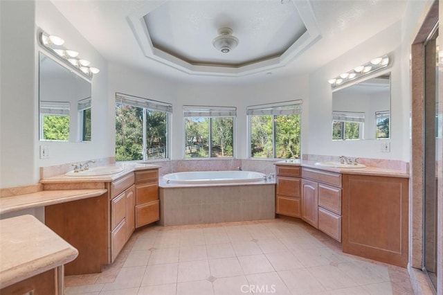 bathroom featuring a relaxing tiled tub, vanity, a wealth of natural light, and a raised ceiling