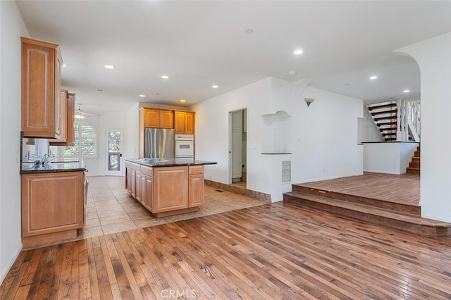 kitchen with white oven, stainless steel fridge, a kitchen island, and light wood-type flooring