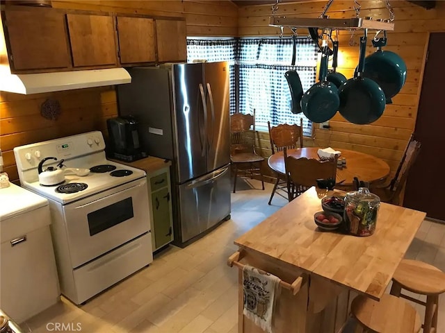 kitchen with white electric stove, stainless steel refrigerator, white cabinets, and wood walls