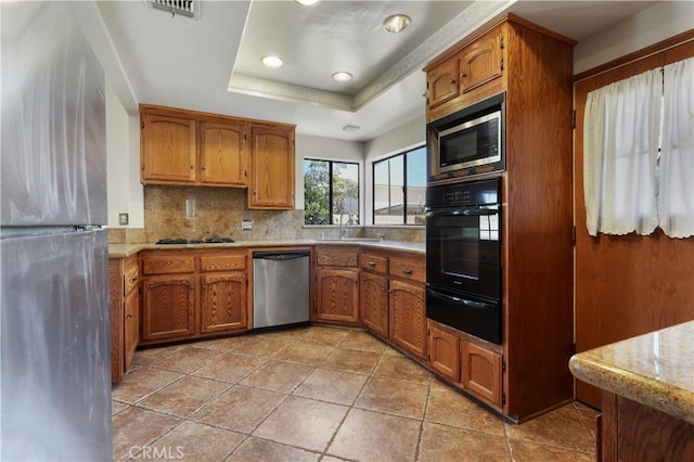 kitchen with appliances with stainless steel finishes, sink, decorative backsplash, light tile patterned floors, and a raised ceiling