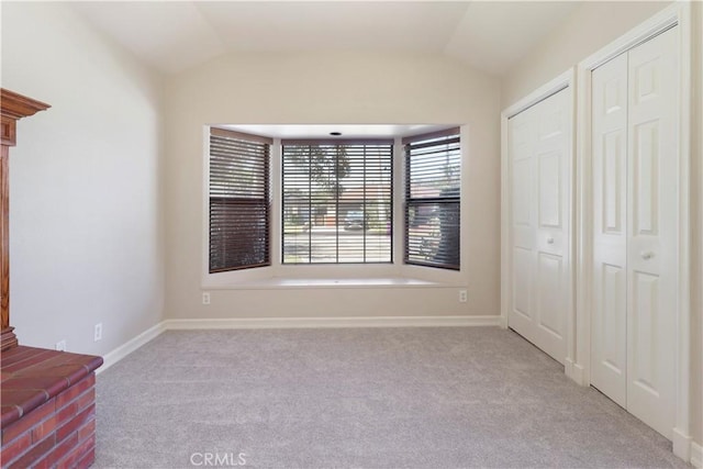 unfurnished bedroom featuring multiple closets, light colored carpet, and vaulted ceiling