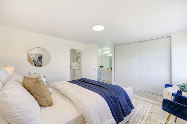 bedroom featuring a closet, ensuite bathroom, and light hardwood / wood-style flooring