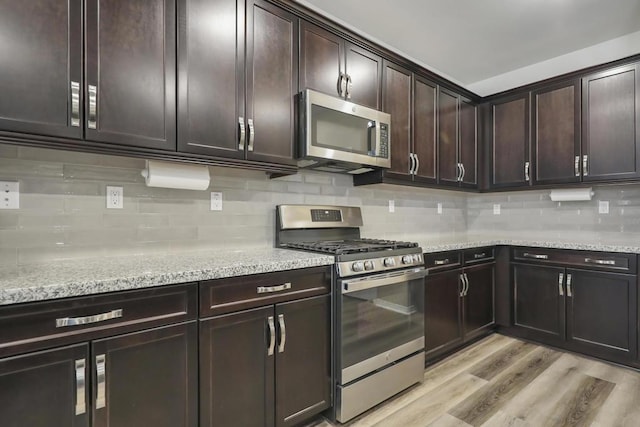 kitchen featuring appliances with stainless steel finishes, backsplash, light stone counters, dark brown cabinetry, and light hardwood / wood-style floors