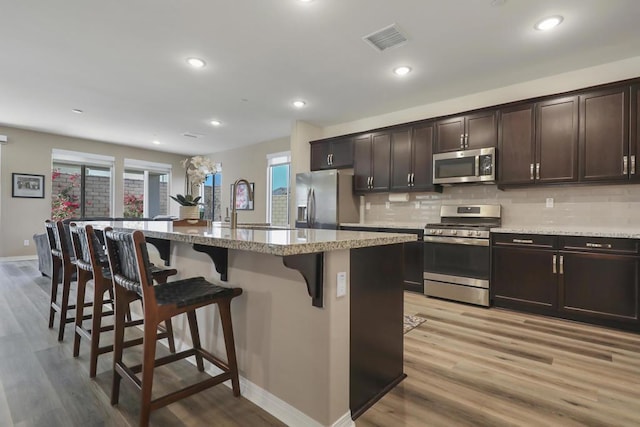 kitchen featuring stainless steel appliances, dark brown cabinets, a breakfast bar area, and a center island with sink