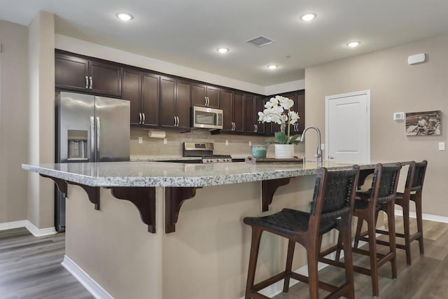 kitchen featuring decorative backsplash, stainless steel appliances, an island with sink, and a kitchen bar