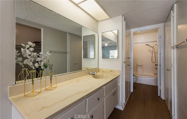 full bathroom with hardwood / wood-style floors, vanity, shower / bathing tub combination, a textured ceiling, and toilet