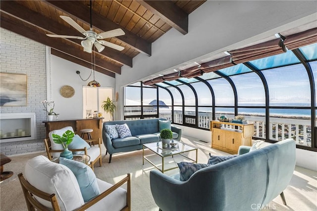 sunroom featuring vaulted ceiling with beams, ceiling fan, wood ceiling, a water view, and a brick fireplace