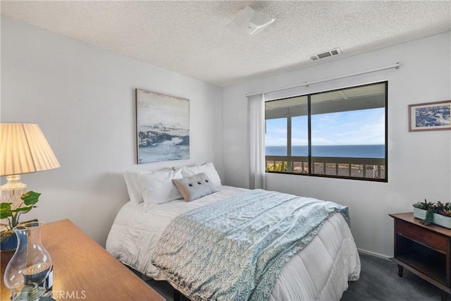 carpeted bedroom featuring a water view, visible vents, and a textured ceiling