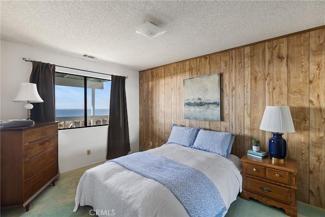 bedroom featuring a textured ceiling, wooden walls, visible vents, and carpet flooring