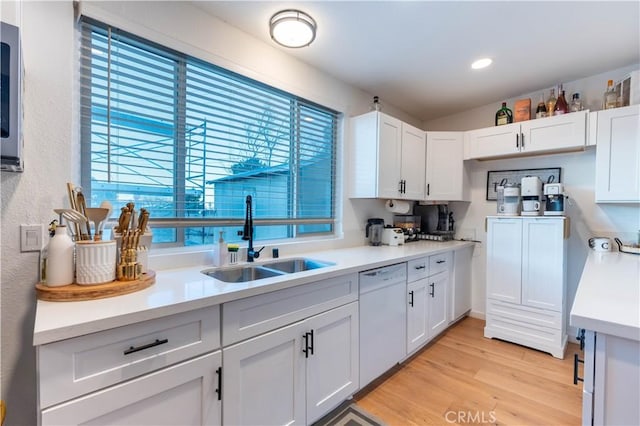 kitchen featuring sink, vaulted ceiling, dishwasher, light hardwood / wood-style floors, and white cabinets