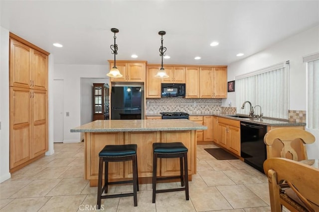 kitchen featuring decorative light fixtures, sink, a center island, black appliances, and light stone countertops