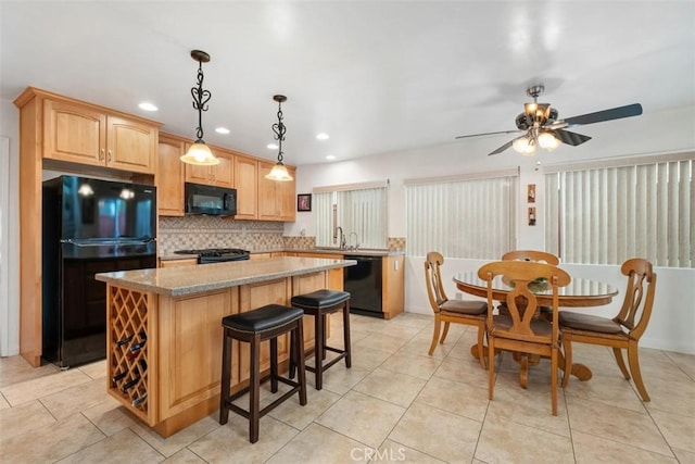 kitchen with sink, hanging light fixtures, a center island, light stone counters, and black appliances