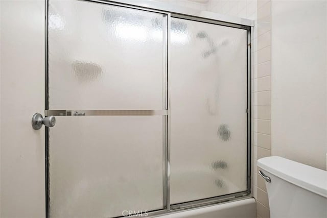 bathroom featuring bath / shower combo with glass door and toilet