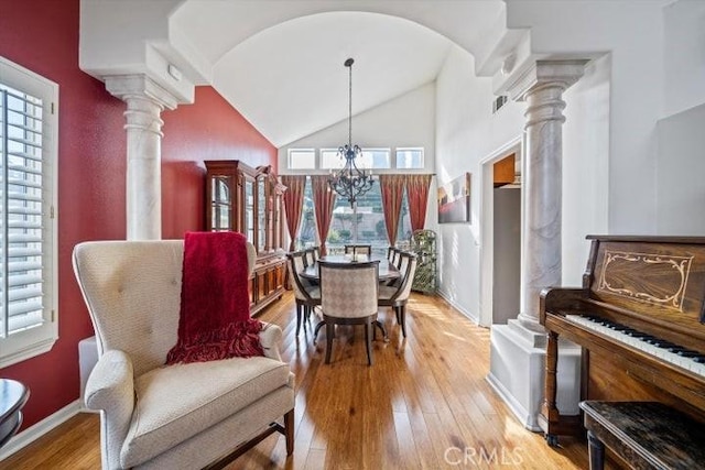 dining space with ornate columns, high vaulted ceiling, an inviting chandelier, and light hardwood / wood-style flooring