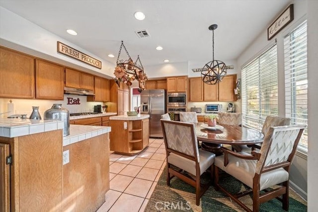 kitchen featuring light tile patterned floors, stainless steel appliances, a kitchen island, decorative light fixtures, and tile countertops