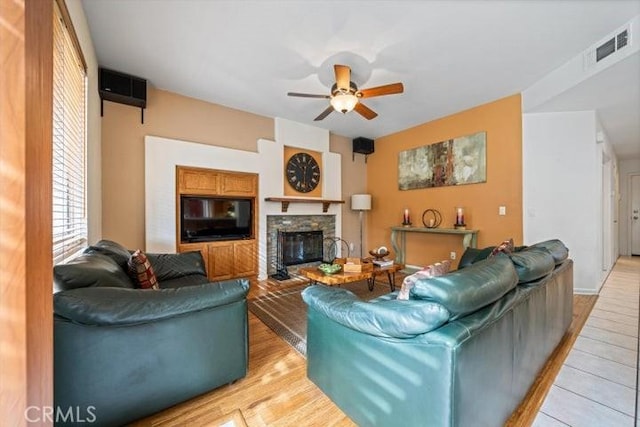 living room featuring ceiling fan, a stone fireplace, and light wood-type flooring