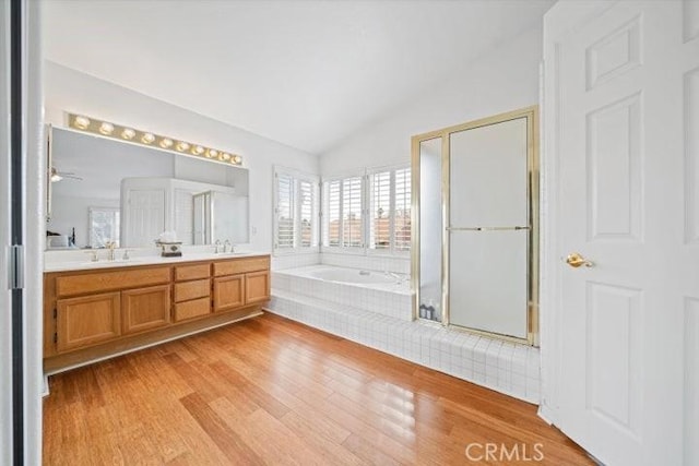 bathroom with lofted ceiling, tiled tub, vanity, and hardwood / wood-style floors