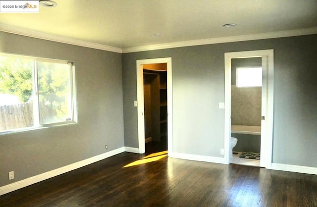 unfurnished bedroom featuring crown molding, a walk in closet, ensuite bathroom, and dark hardwood / wood-style flooring