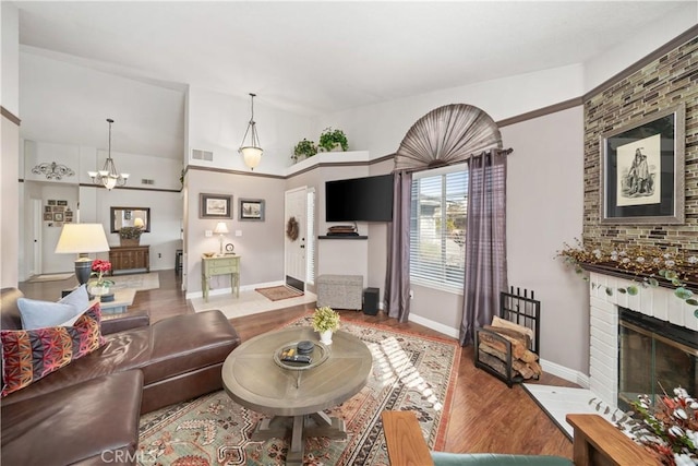 living area with wood finished floors, visible vents, baseboards, a brick fireplace, and an inviting chandelier