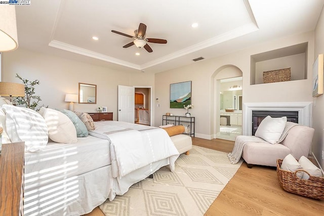 bedroom with connected bathroom, light hardwood / wood-style floors, and a tray ceiling