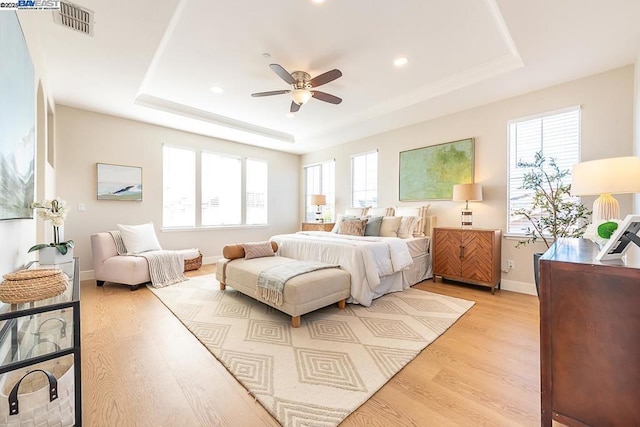 bedroom with a tray ceiling, light hardwood / wood-style floors, and ceiling fan