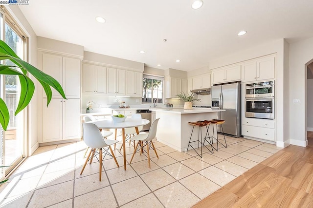 kitchen with a breakfast bar, sink, white cabinets, a center island, and stainless steel appliances