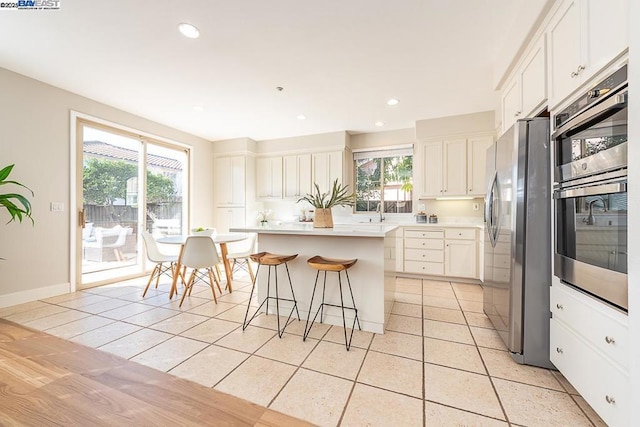 kitchen with light tile patterned flooring, white cabinetry, a kitchen breakfast bar, a kitchen island, and stainless steel appliances