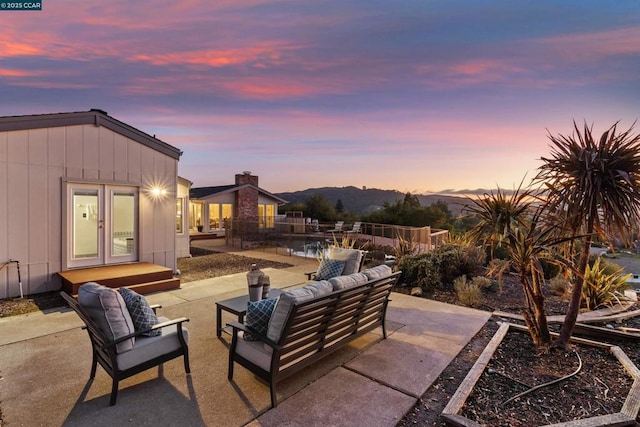 patio terrace at dusk featuring a mountain view, outdoor lounge area, and french doors