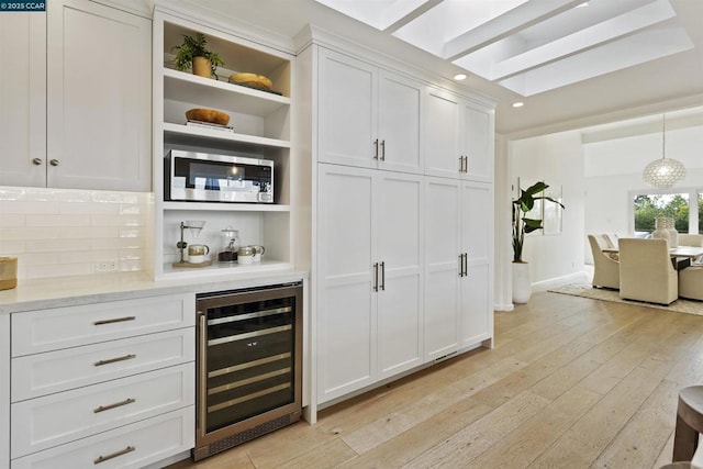 bar featuring pendant lighting, white cabinetry, backsplash, beverage cooler, and light wood-type flooring