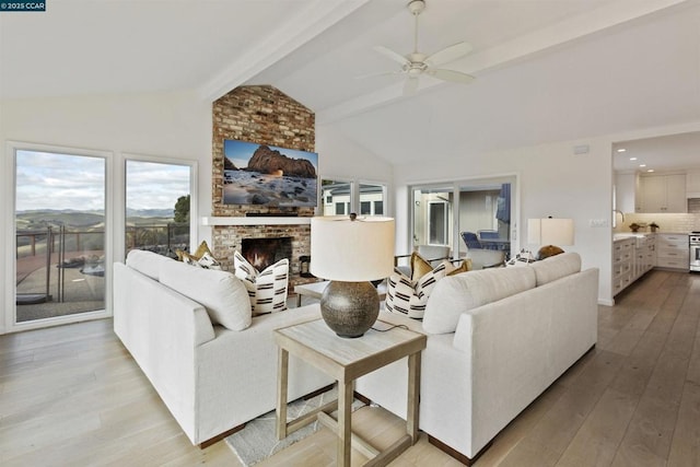 living room with ceiling fan, vaulted ceiling with beams, a fireplace, and light hardwood / wood-style flooring