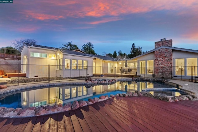 pool at dusk featuring a wooden deck and an in ground hot tub