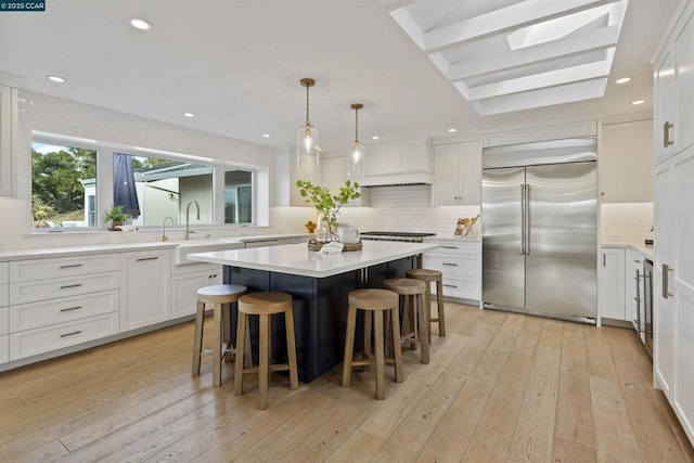 kitchen with white cabinetry, built in refrigerator, sink, and a kitchen island