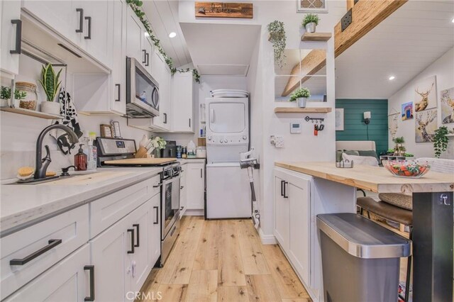 kitchen with stainless steel appliances, stacked washing maching and dryer, and white cabinets